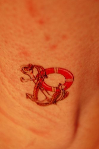 Tattoo von rotem Schiffanker in der Knöchelgegend