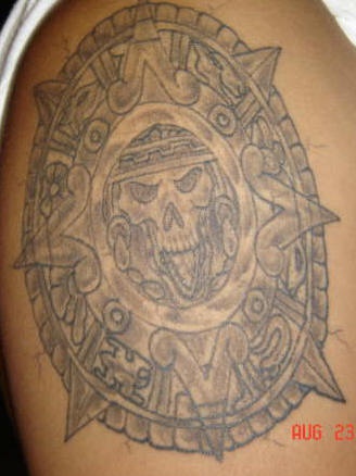 Tatuaje en el hombro de un calendario de muerte de estilo azteca.
