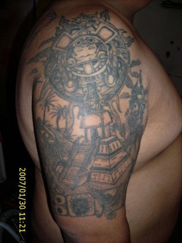 Tatuaje en el hombro del sol en piedra y una pirámide azteca.