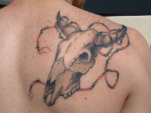 Tatuaje en el hombro de un cráneo de toro con alambre de puas.