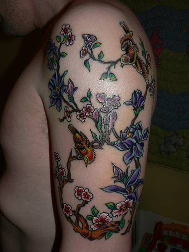 Tatuaje en el brazo, rama con montón de flores y aves en elle dibujo multicolor