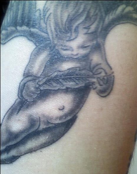 Tatuaje en tinta negra de angelito con una  pluma en las manos