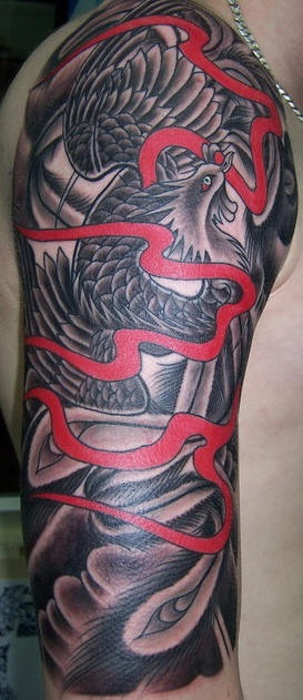 el tatuaje de un ave Fenix en tinta negra con una liston rojo  hecho en el brazo