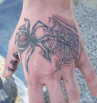 Tatuaje en tinta negra araña con teleraña en la mano