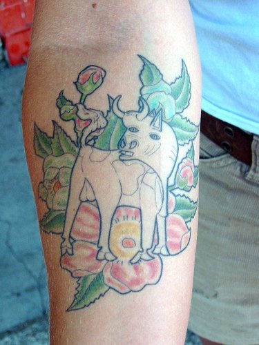 Funny white bull on flowers arm tattoo