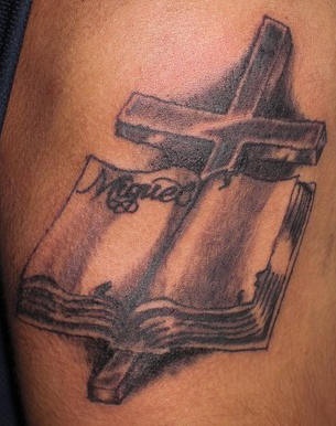el tatuaje conmemorativo de una cruz con un libro y el nombre escrito en el hecho en color negro