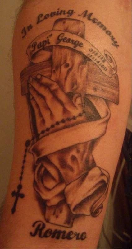 el tatuaje conmemorativo con las manos orantes, una cruz de madera y un rosario
