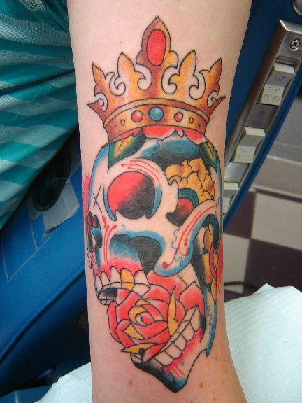 cranio colorato con rosa in bocca e corona sulla cima tatuaggio