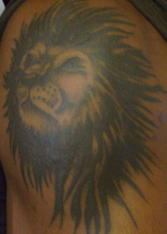 El tatuaje de la cabeza de un leon negro con melena grande en el hombro
