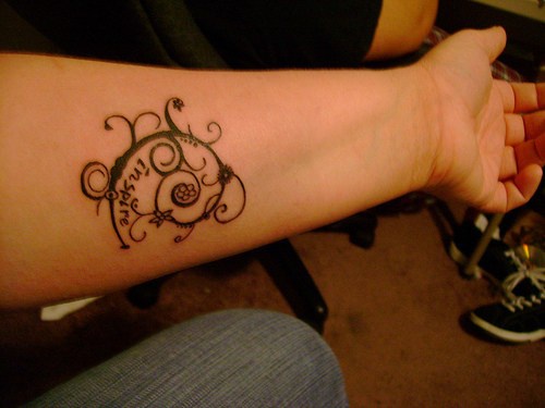 Tattoo von geschnörkeltem Zeichen und Aufschrift am Unterarm