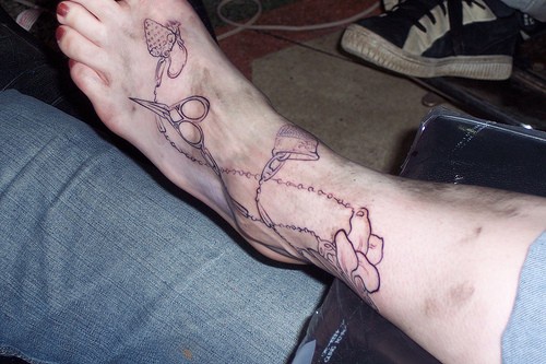 Chaînes avec des ciseaux et doigtier le tatouage sur le pied