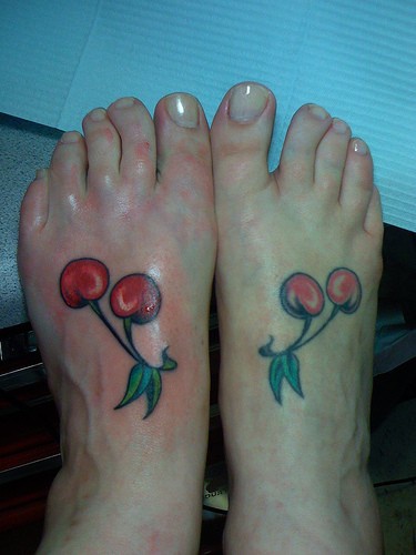 Dos cerezas con hojas verdes tatuados en cada pie