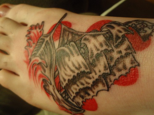 Le navire dans les vagues rouges le tatouage sur le pied