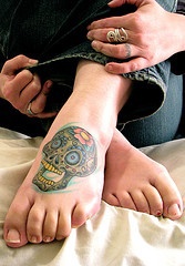 Tatuaje en el pie, cráneo abigarrado que se rie con la boca abierta