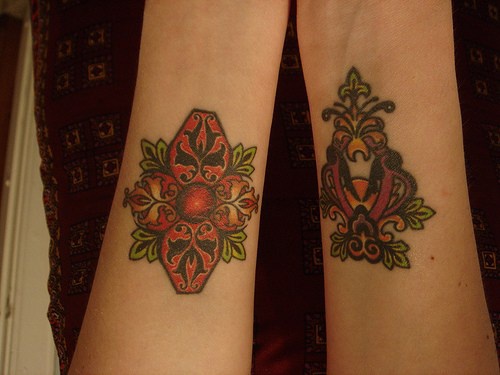 Tattoo von zwei malerischen Zeichen mit Blättern und Schnörkeln am Unterarm