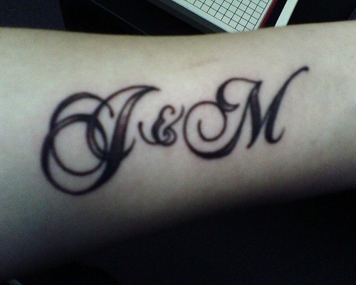 Tatuaje en el antebrazo, dos letras, fuente especial, cursiva