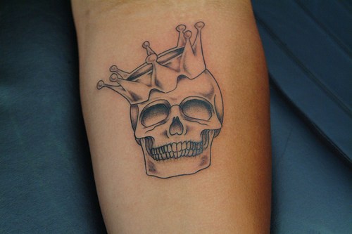 Colorless laughing skull with crown forearm tattoo