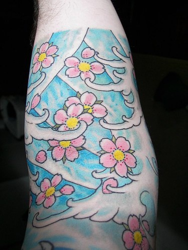 Tatuaje en el antebrazo, bonitas flores pequeñas de color rosa sobre un fondo azul