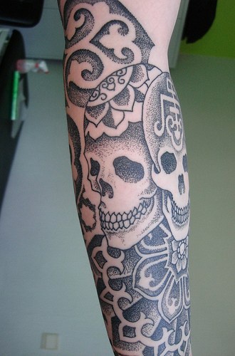 Tatuaje en el antebrazo, dos esqueletos sobre un fondo de ornamento