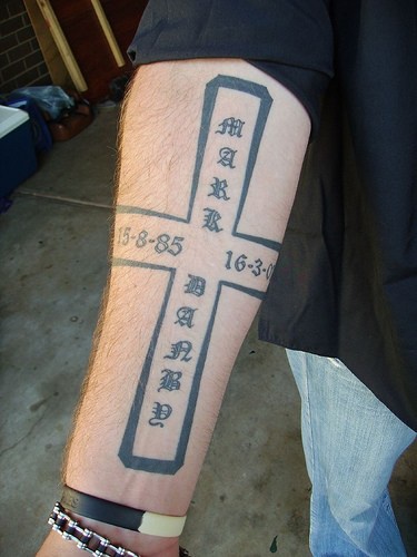 Three-dimensional cross with signs forearm tattoo