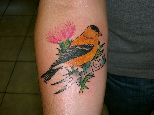 Tattoo von gelbem Vogel, Blume und Aufschrift &quotMom" am Unterarm