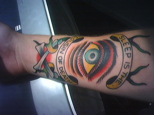 Tatuaje en el antebrazo, un ojo grande, frase el sueño es el primo de la muerte