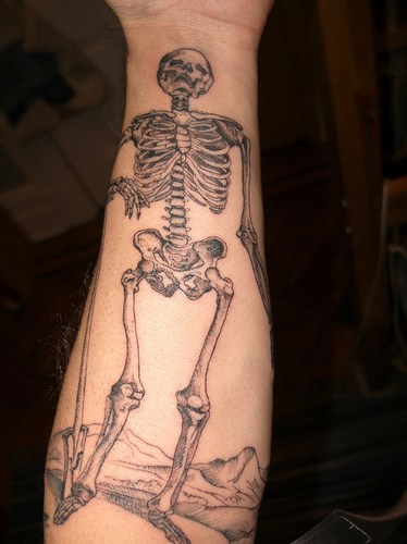 Tatuaje en el antebrazo, esqueleto en el fondo de montañas