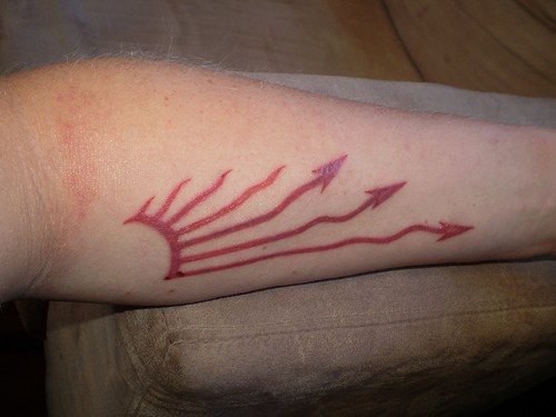 Red image with  waving arrows forearm tattoo