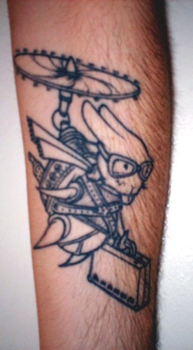 Tatuaje en el antebrazo, conejo con la hélice sostiene la maleta, diseño descolorido