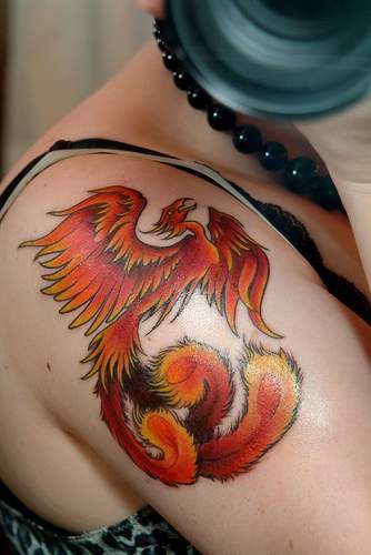 el tatuaje hermoso de la ave fenix de color naranja hecho en el hombro