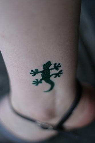 El tatuaje pequeño de una lagartija negra en la pierna