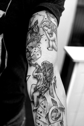 Dice cards and cherubs tattoo on arm