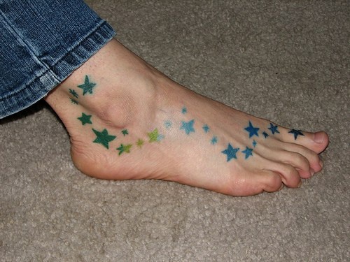 tatuaje femenino en el pie de estrellas coloridas