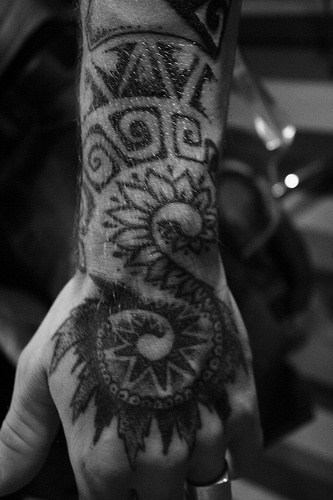 Tattoo von malerischen Figuren, Blättern, Schnörkeln  an der Hand