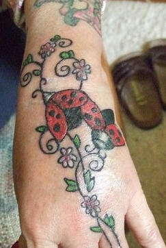Tatuaje en la mano, mariquita que se siete en la rama con flores