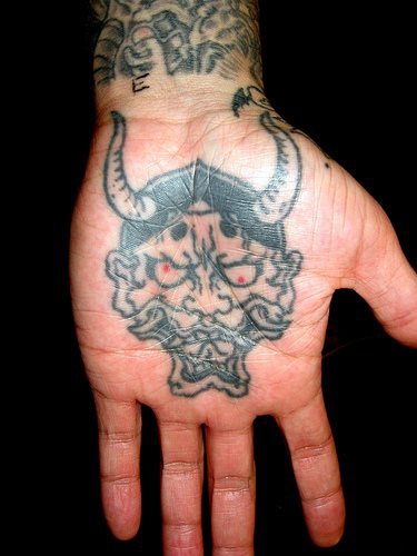 Tatuaje en la mano, demonio cornudo, con la boca abierta