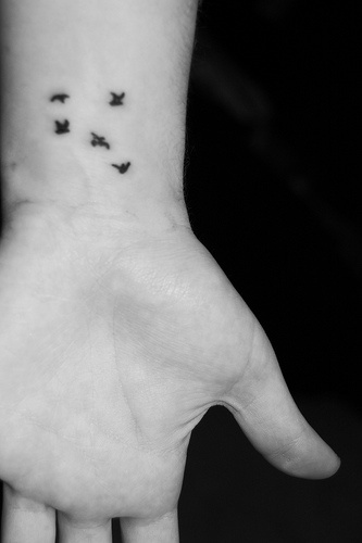Tattoo von kleinem fliegendem Vogelschwarm in Schwarz an der Hand