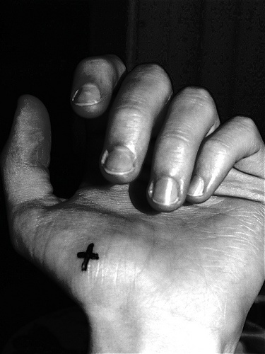 Tattoo von winzigem fettbedrucktem Kreuz in Schwarz an der Hand