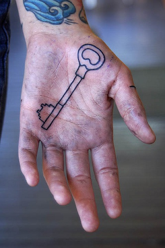Nichtfarbiges Tattoo von einem langen Schlüssel an der Handfläche