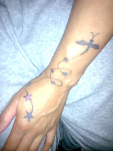 Delicato tatuaggio sul braccio: la libellula e le stelle sul filo