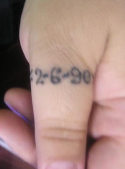 Tattoo von als ein Ring auf dem Daumen gestalteten Zahlen in Schwarz