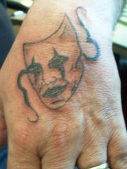 Nichtfarbiges Tattoo von trauriger Maske an der Hand