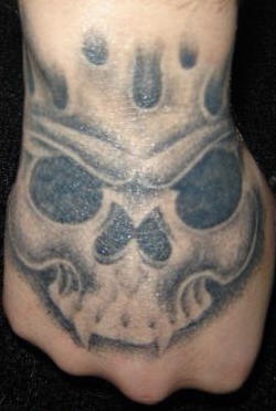 Tatuaje en la mano, cráneo con colmillos sin ojos y nariz
