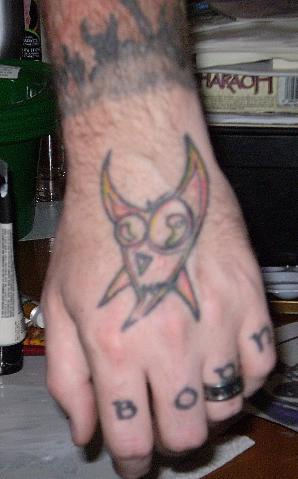 Tattoo von horniger Mieze an der Hand und einem Namen an Fingern