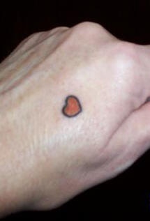 Tatuaje en la mano, corazón rojo con contornos negros, diseño muy diminuto