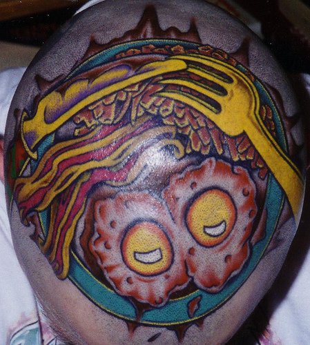 Tattoo von stilisiertem Essen, Spiegeleier und Gabel auf dem Kopf