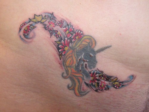 Tatuaje en la cadera, unicornio con el cabello dorado y flores multicoles