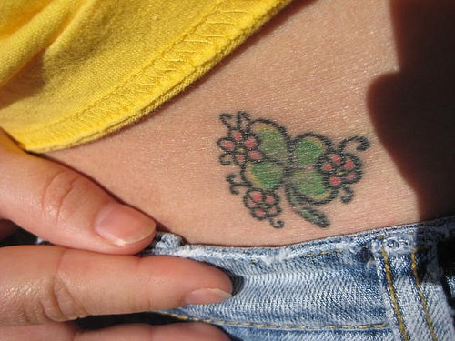 Un petit trèfle vert avec des fleurs tatouage sur la hanche