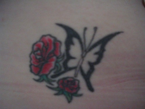 Tatuaje en la cadera, mariposa descolorida con dos flores rojos