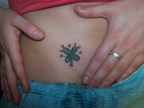 Tattoo von kleinem grünem schönem Kleeblatt mit einem Namen an der Hüfte